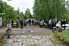 Folk samlet ved parkerte motorsykler på en steinlagt gårdsplass med trær og busker rundt.