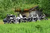 Flere motorsykler står parkert i et grønt gressområde foran et gammelt skur.