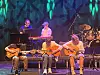 Band opptrer på en scene med gitarer, keyboard og trommer under blå og grønne lys.