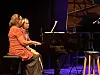 To kvinner sitter ved et svart Bechstein-flygel på en scene med blå og lilla lys.