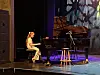 En pianist sitter ved et svart flygel på en mørk scene med lilla belysning.