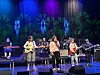 Et band opptrer på en scene med fargerike lys og musikkinstrumenter.