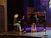 Pianist ved et flygel på en scene med blå og lilla lys.