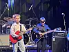 To unge gitarister spiller foran et trommesett på en konsertscene.