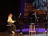 Ung pianist spiller ved et Steinway-flygel på en scene med mikrofon og krakk ved siden av.