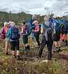 Ei gruppe turgåere med sekker står samlet i et myrlandskap med skog i bakgrunnen.