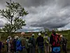 Turgåere med ryggsekker står på en høyde og ser utover et landskap under overskyet himmel.