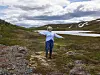 En person med utstrakte armer står på en sti i et fjellandskap med snø og vann.