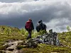 To turgåere med ryggsekker går over en steinete fjellrygg under dramatiske skyer.