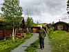 Mann står ved en grussti ved siden av trehytter og grønne åser.
