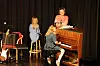 Tre personer på en liten scene med gitarer og piano under varmt lys.