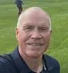Mann tar selfie på en fotballbane med en spiller i bakgrunnen.