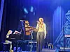 Artist synger på en scene med piano, mikrofonstativ og blå belysning.