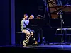 Unge pianister ved et svart flygel på en scene med blått lys.