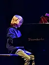 Ung pianist sitter ved et svart Bösendorfer-flygel på en mørk scene.