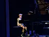 Ung pianist sitter ved et svart flygel på en mørk scene.