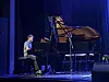 En pianist ved et svart flygel på en scenen med blått lys.
