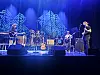 Band spiller på en blå opplyst scene med gitarer, trommer og mikrofoner.