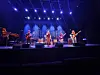 Band spiller på en scene med sterke blå og lilla lys foran et mørkt publikumsområde.