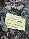 Gul lapp med rød håndskrift ligger mellom steiner ute.