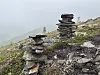 Flere små varder av stein står på en steinete fjellside i tåke.