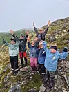 Seks turkledde barn står på en steinete fjellrygg med armene i været i tåke og fjellandskap.
