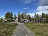 Folk står og går mellom lavvoer, trebygninger og et åpent uteområde på en solrik dag.