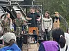 Flere personer står på en enkel utendørsscene mens publikum ser på foran.