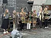 Flere utkledde barn utendørs foran en bygning. De klapper i hendene.