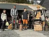 Fire personer står fremst med rekvisitter utendørs. Musikkinstrumenter/utstyr bak.