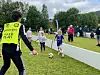 Barn spiller fotball på en gressbane mens en ungdom  i gul vest er dommer nærmest kameraet.