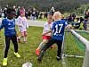 Barn i fotballdrakter spiller nær et mål på en gressbane med tilskuere i bakgrunnen.
