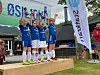 Barn i fotballdrakter står på en premiepall og jubler under premieutdeling utendørs.