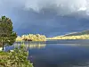 Stille fjellvann, mørke skyer, trær og skog.