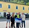 En liten gruppe mennesker står foran en gul bygning mens en person holder en stor gavesjekk.