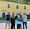 Seks personer står foran et gult bygg og holder et skilt med Sparebank 1 -logo.