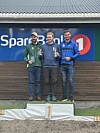 Tre menn står på en seierspall, med nummer 1 i midten.