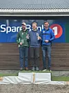 Tre menn står på en seierspall, med nummer 1 i midten.