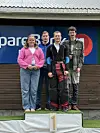 Fire ungdommer står sammen på en seierspall foran et stort sponsorbanner.