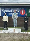 Tre personer står på en seierspall foran et SpareBank 1 Nordmøre-skilt utendørs.