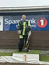 En person står på en seierspall med trofé foran et SpareBank 1-skilt.