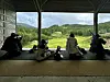 Tre personer og sykler under et overbygd utsiktspunkt med grønt landskap bak.