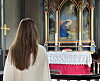 En kvinne sett bakfra står foran et utsmykket alter i en kirke.