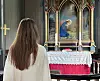 En kvinne sett bakfra står foran et utsmykket alter i en kirke.