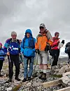 Fire turgåere står på en steinete fjelltopp under en overskyet himmel.