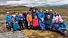 En gruppe turgåere står samlet i et åpent høyfjellslandskap med fjell og skyet himmel.
