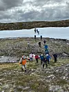 Flere turgåere krysser et snøfelt mellom steinete partier i et fjellområde.