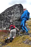 To personer i turklær ved en stor steinblokk i et røft fjellterreng.