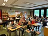 Elever sitter ved pulter i et klasserom med tavler, kart og oppslag på veggen.