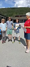Tre barn og en kvinne står på en skolegård, og ett barn holder et diplom.